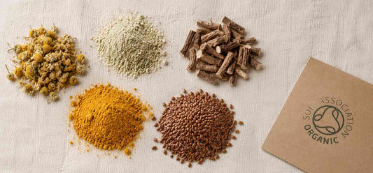 bright turmeric powder, and bronze flaxseeds, with a kraft paper card showing the Soil Association certified organic logo to the right.
