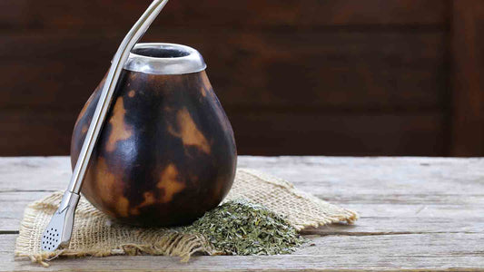 Traditional yerba mate gourd and bombilla with loose yerba mate leaves on a rustic wooden table.