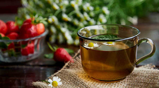 A glass cup full of chamomile tea with strawberrys in the background.
