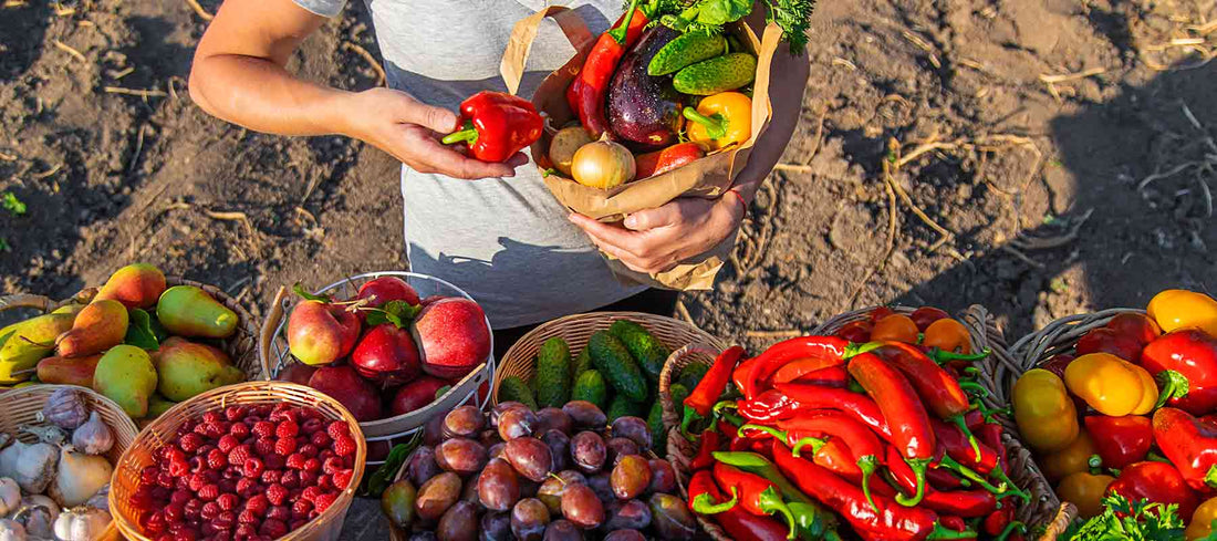 A woman buying brightly coloured fruit and vegetable from an ourdoor market.