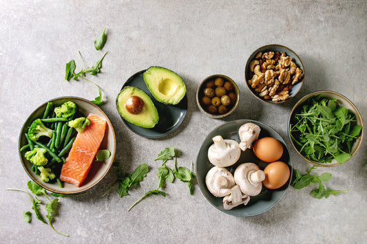 Keto diet approved foods including salmon, avacado, mushrooms and beans on a grey background.