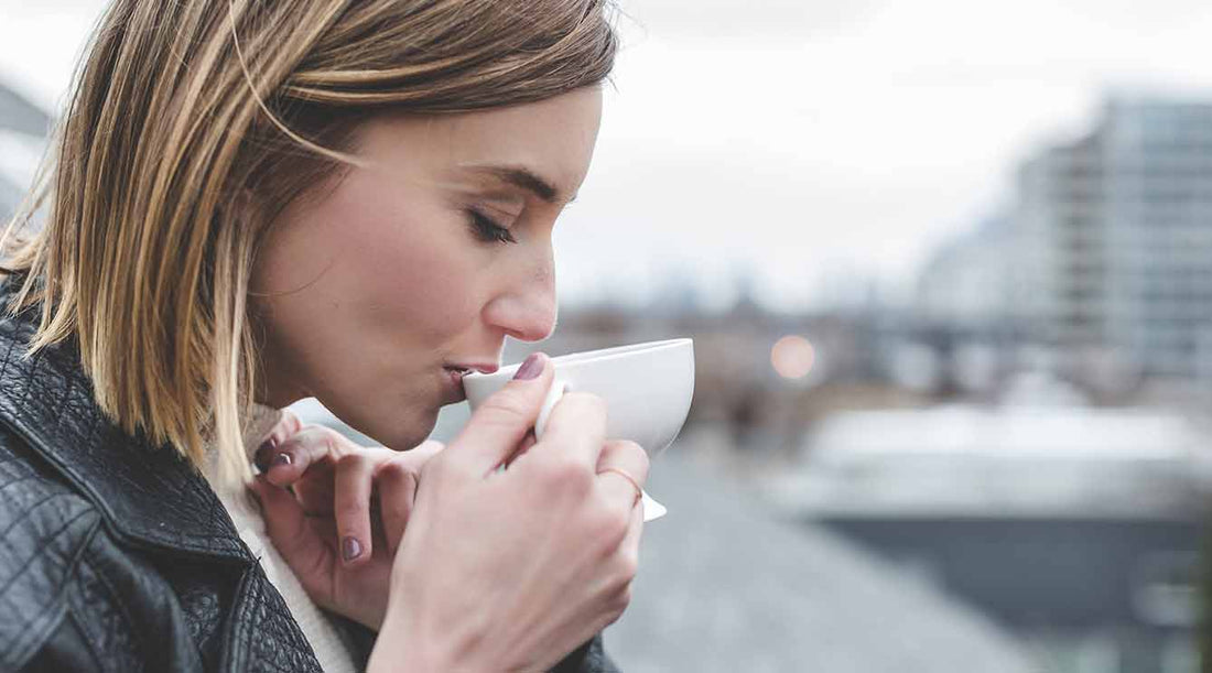 A girl with bobbed blond hair mindfully drinking tea by a river.