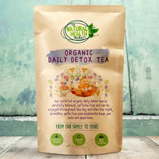 Kraft paper packaging of Organic Daily Detox Tea from The Natural Health Market on a wooden surface with a blurred green background.