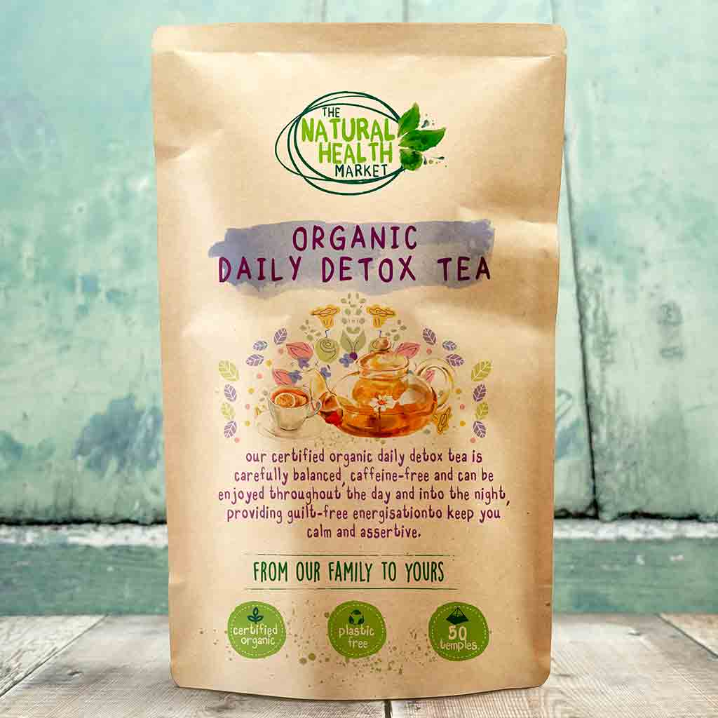 Kraft paper packaging of Organic Daily Detox Tea from The Natural Health Market on a wooden surface with a blurred green background.