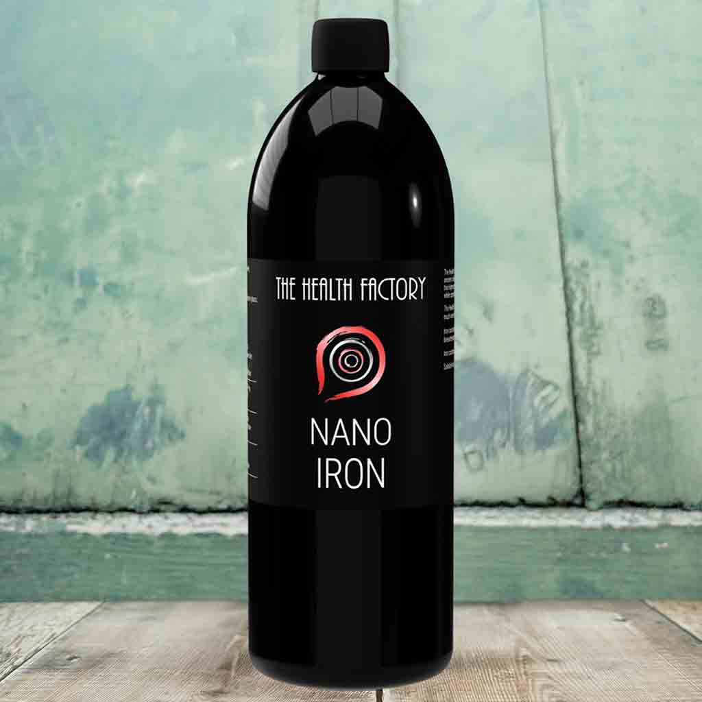 Black bottle labeled 'Nano Iron' from 'The Health Factory' on a wooden surface with a greenish background.