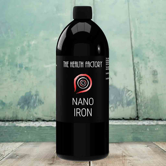 Black bottle labeled 'The Health Factory Nano Iron' on a wooden surface with a greenish background.