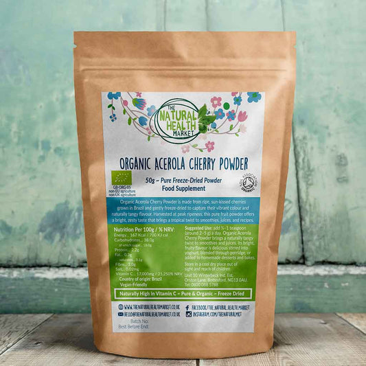 Package of Organic Acerola Cherry Powder 50g from The Natural Health Market on a wooden surface with a blurred green background.