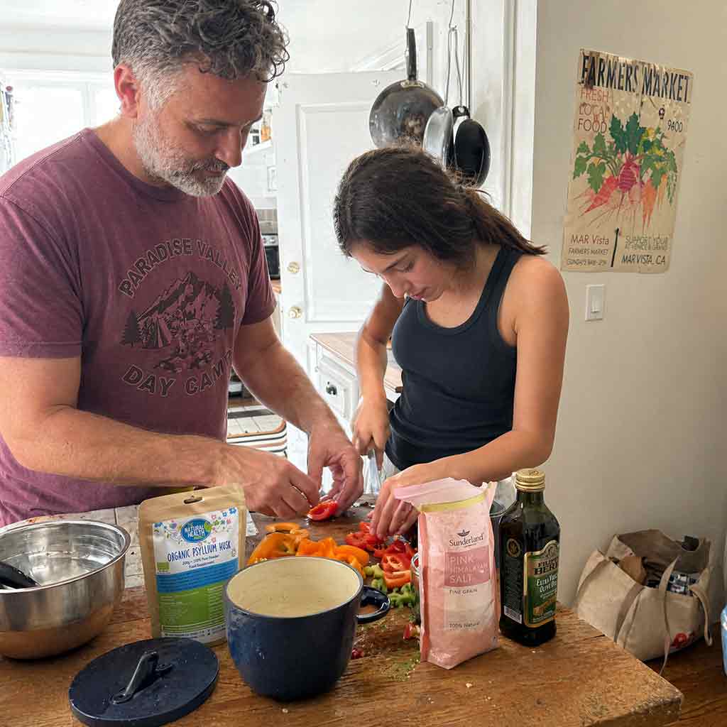 Two people are preparing food in a kitchen with organic psyllium husk and utensils on the counter.
