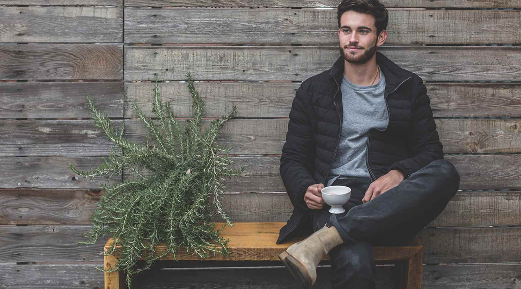 A millennial boy sad outside next to an aloe vera plant enjoying a cup of hibiscus tea.