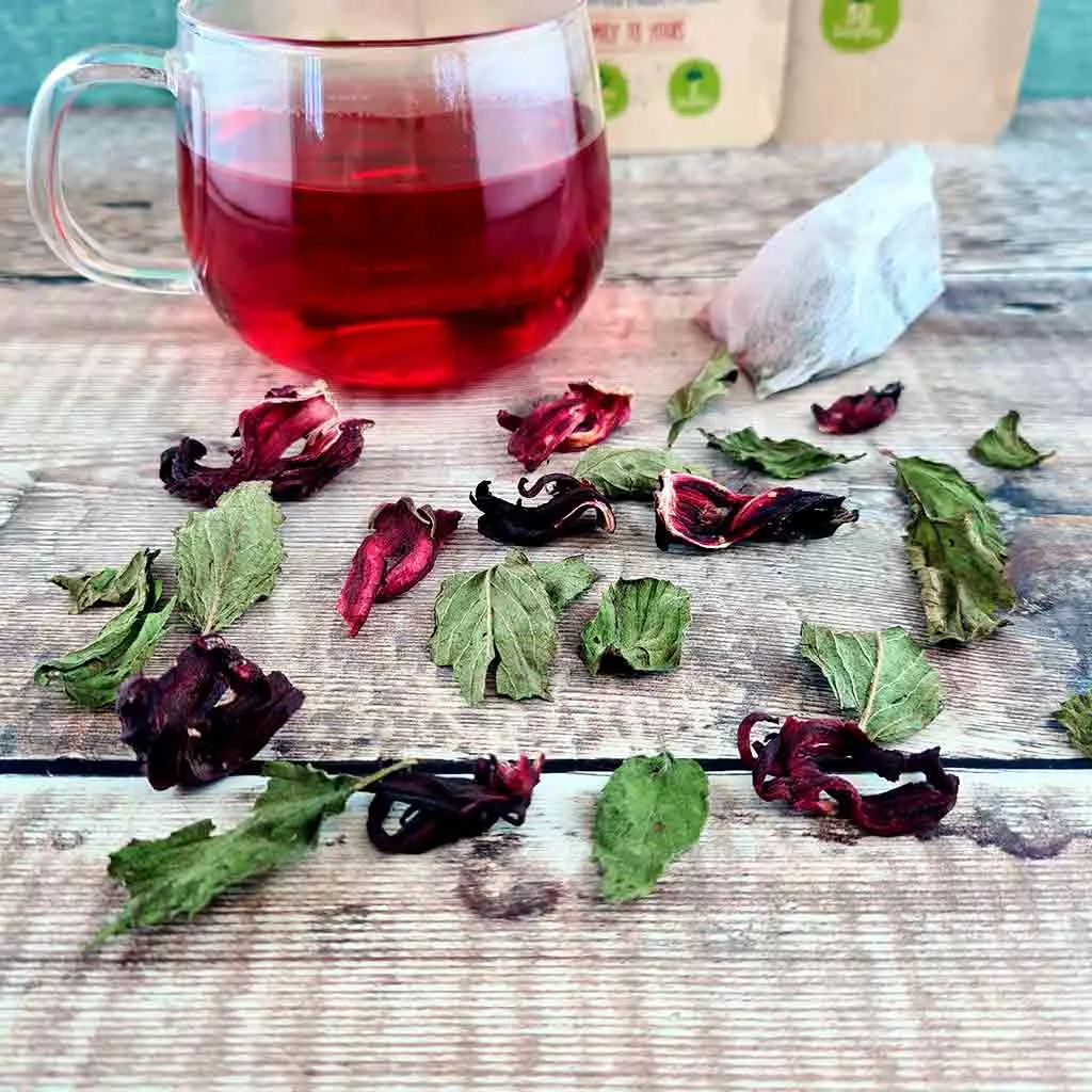 Dark red herbal tea surrounded by hibiscus leaf and peppermint leaves.