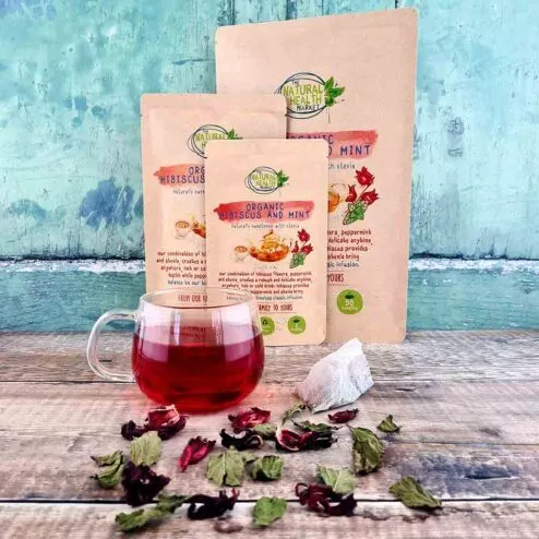 Three packets of hibiscus and mint tea bags with a full tea cup and loose hibiscus and peppermint leaves.
