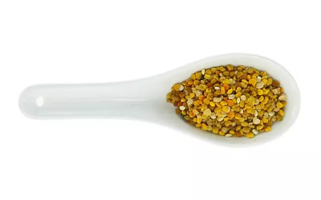 Bee pollen on a white ceramic spoon on a white background.