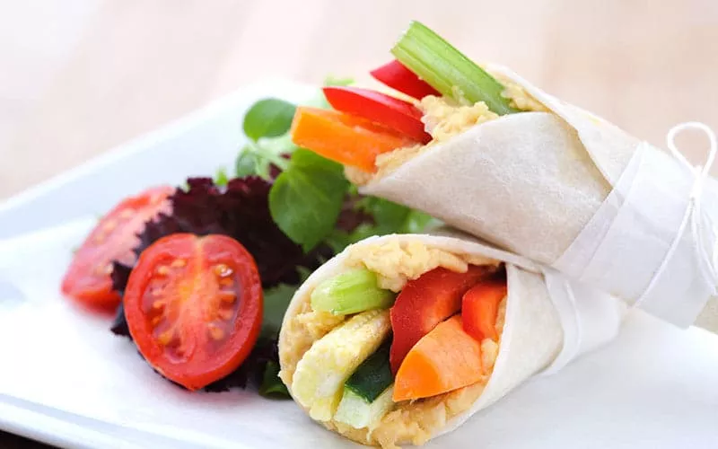 A carrot and hummus wrap on a white plate with a side salad.