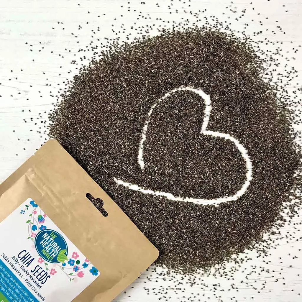 Packet of chia seeds with chia spread out on a white surface with a heart shape drawn into the spilled chia.