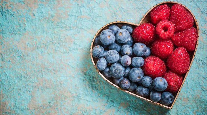 A heart shaped tin half filled with blueberries and half with strawberries.
