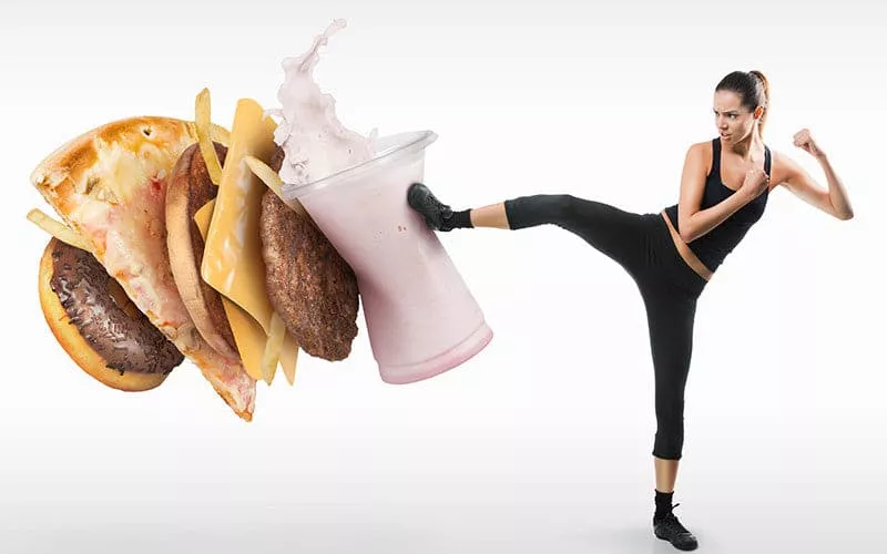 A young lady karate kicking junk food on a white background.