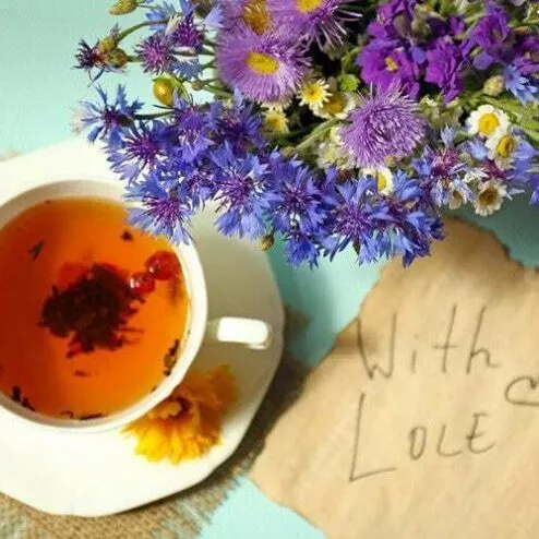 A cup of mulberry tea in a white cup next too a bunch of flowers.