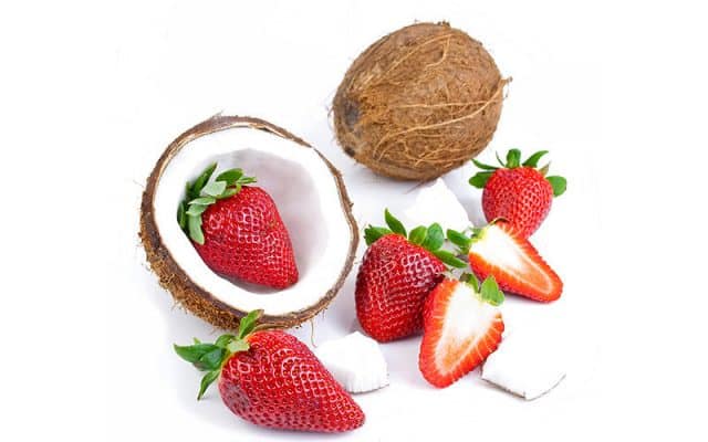 A coconut cut in half along with several fresh strawberries on a white background.
