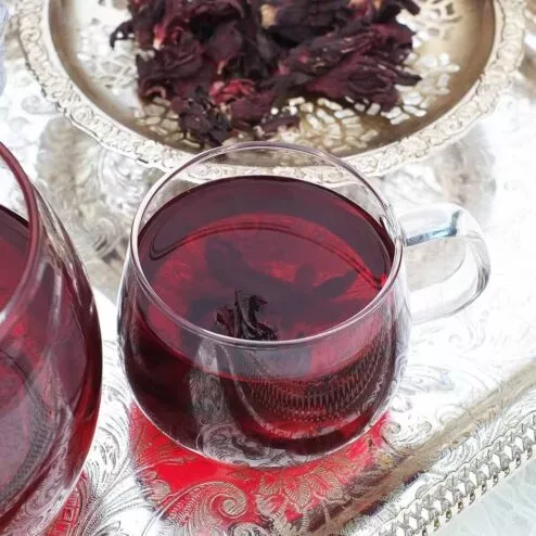 A glass cup full of fresh hibiscus tea on a silver tray.