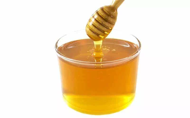 Raw Organic Wild Honey in a glass bowl with a wooden honey spoon.