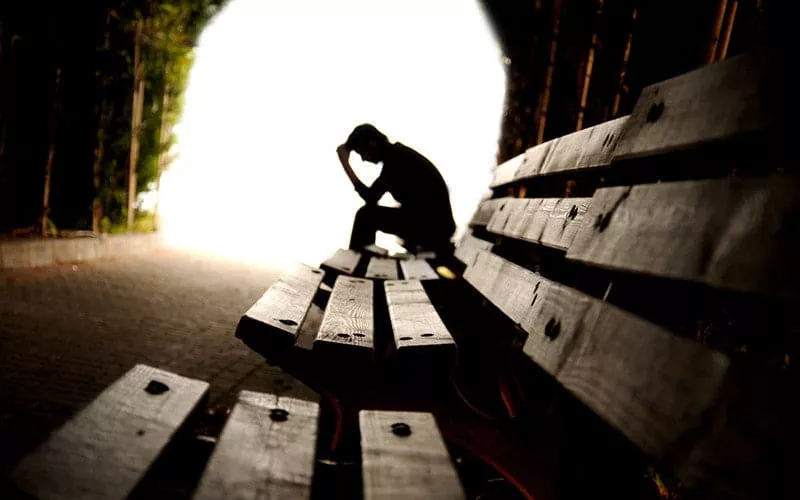 A blurred outline of a man sat at the end of a tunnel on a park bench.