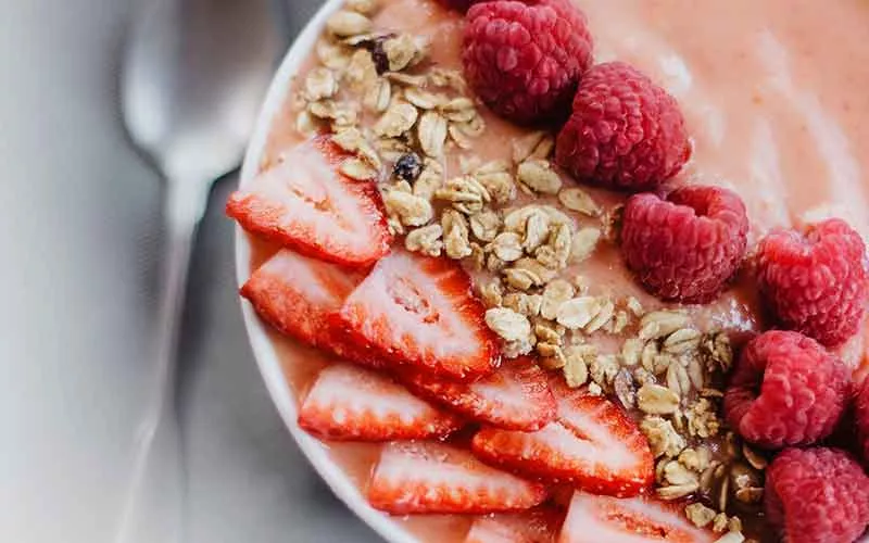 A brightly coloured bowl of muesli decorated with strawberries and raspberries.